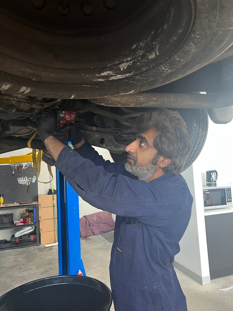 Mechanic working under a vehicle, inspecting or repairing the undercarriage in a garage workshop
