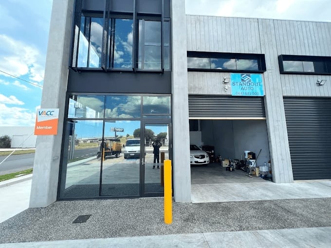 Modern industrial building with glass storefront entrance, yellow bollard, and open garage bay with vehicles visible inside